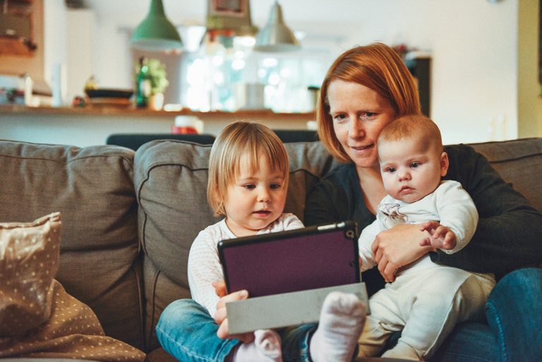 busy mom with two young kids on her lap looking at iPad